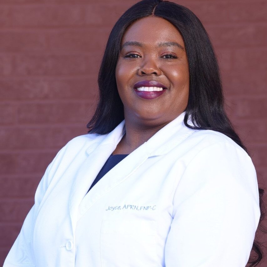 A woman in white lab coat standing next to brick wall.